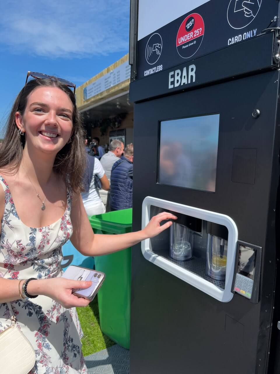 A woman with sunglasses on her head pours herself two pints of lager from a mobile EBar automated beer kiosk