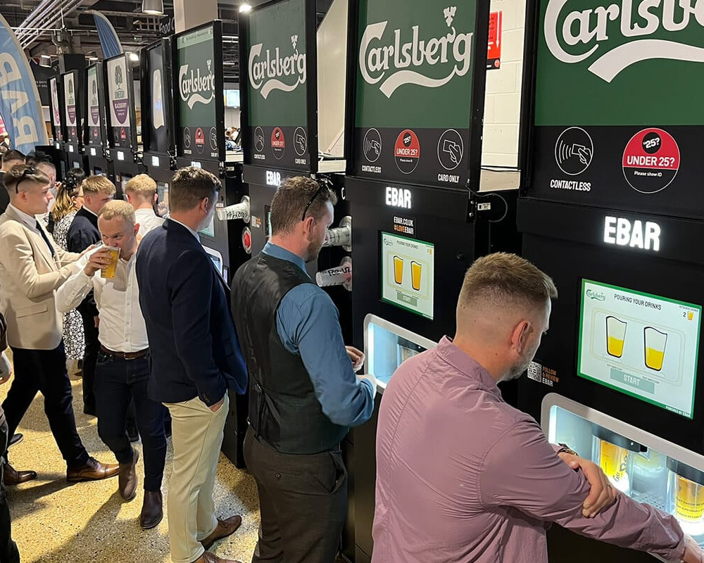 A crowd of racegoers making use of a row of 8 mobile EBar automated beer kiosk units