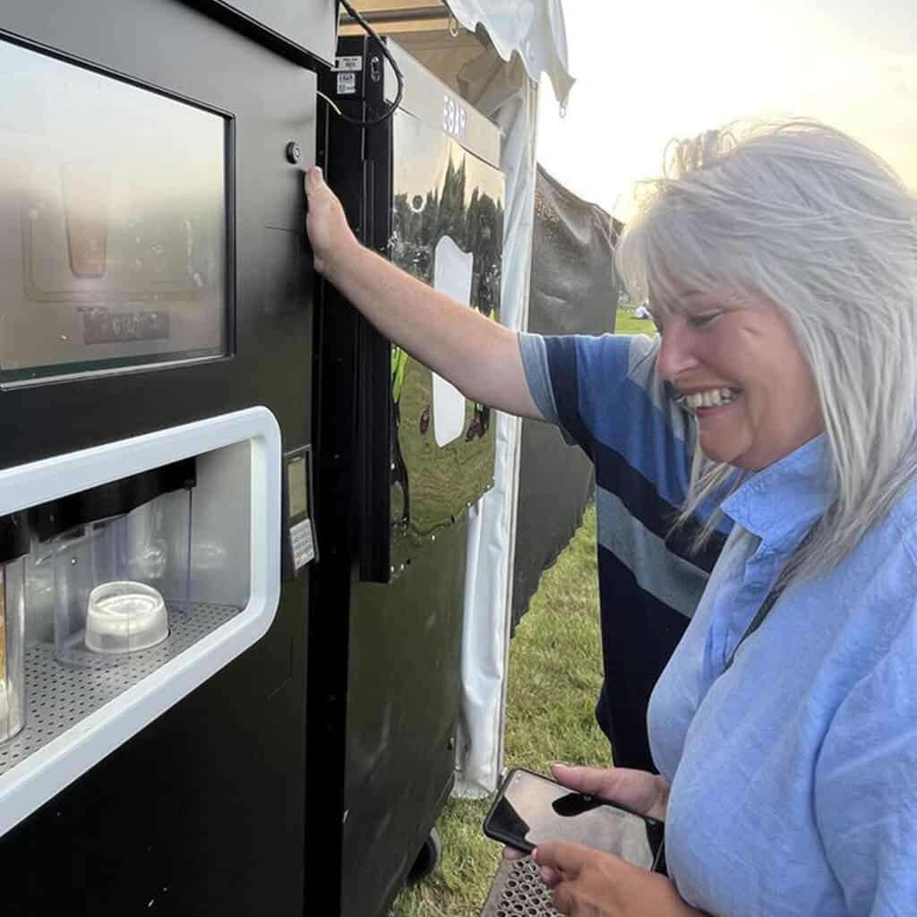A happy woman smiles as she watches her pint being poured by an EBar automated beer kiosk