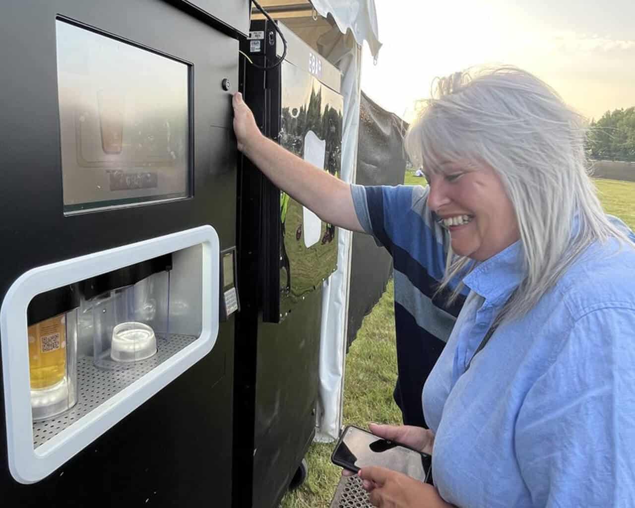 A happy woman smiles as she watches her pint being poured by an EBar automated beer kiosk