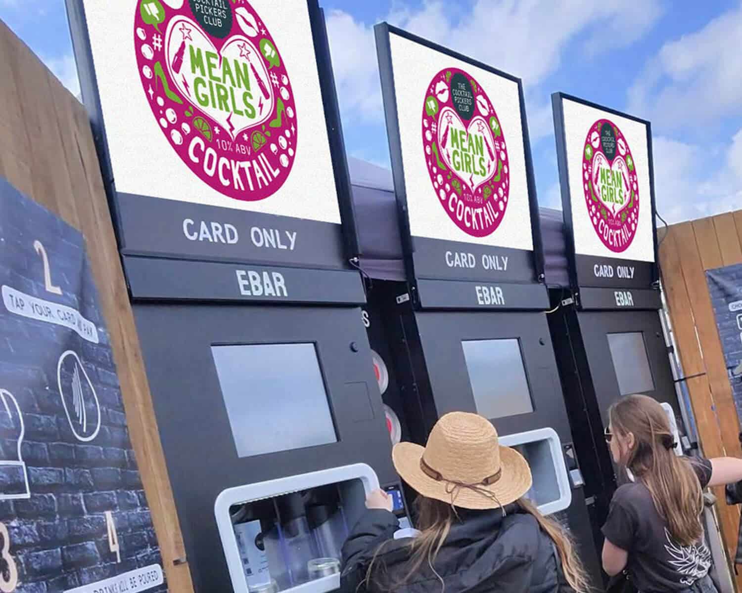 Two women buy cocktails from 3 mobile EBar units with Mean Girls Cocktail branding