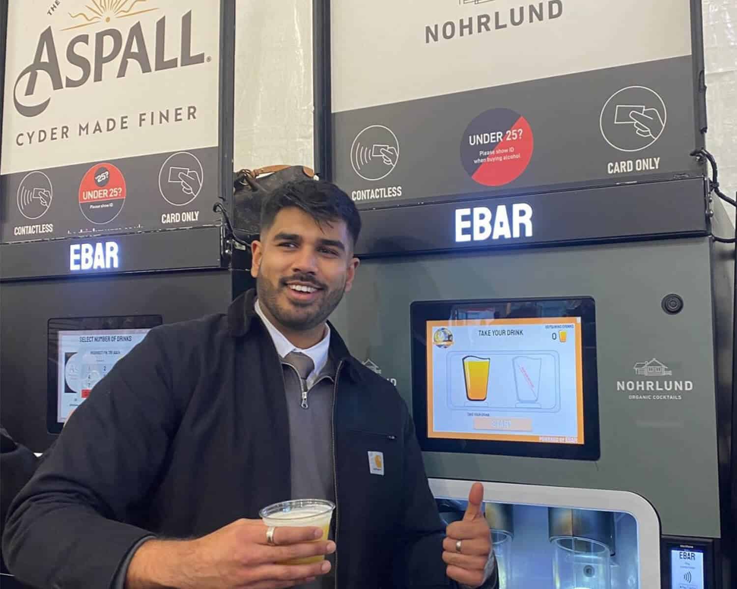 A smiling man gives a thumbs up as he holds a cocktail he just purchased from the mobile EBar unit behind him